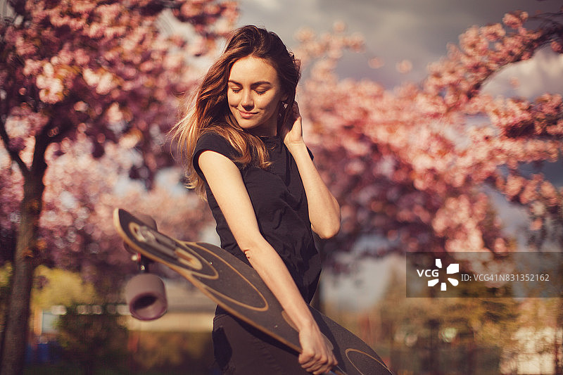 在樱花巷里玩长板的年轻女人图片素材