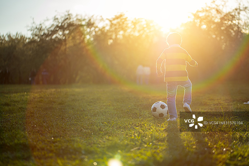 男孩在日落时分的公园里踢足球图片素材