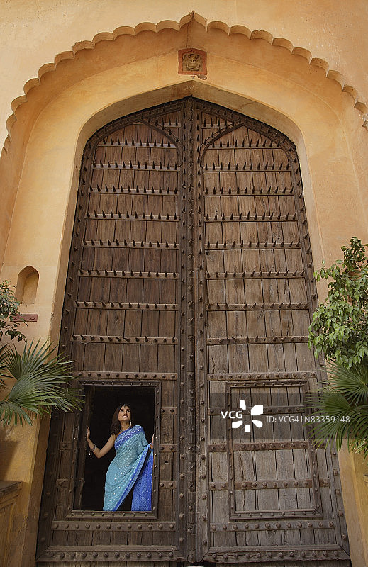 年轻女子站在巨大的木门前图片素材