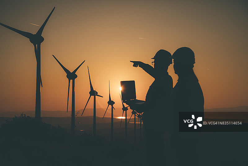 日落时分在风力涡轮机场工作的年轻维修工程师团队图片素材