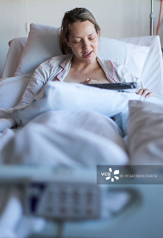 年轻女子用平板电脑填写她在医院分娩的回顾，同时进行母乳喂养图片素材