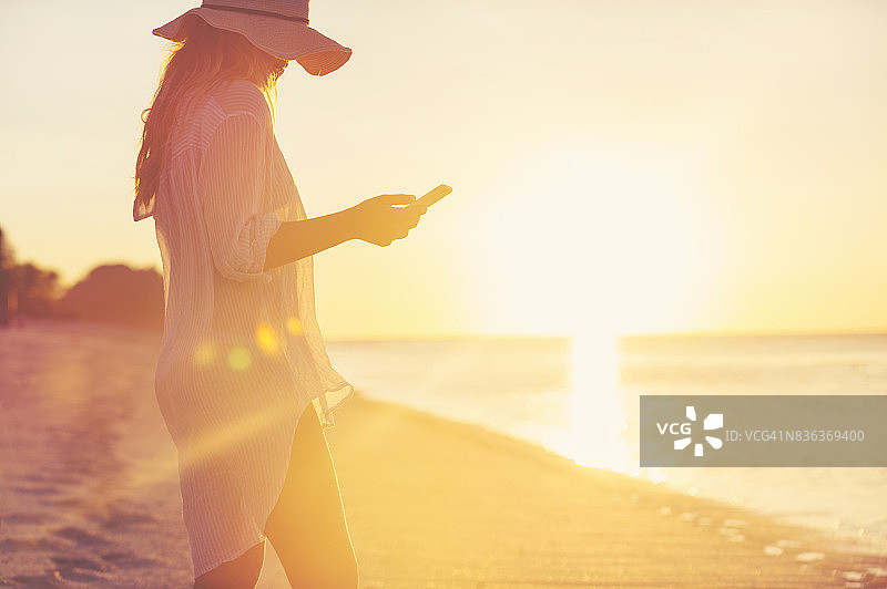 独自在海滩上使用手机的女人图片素材
