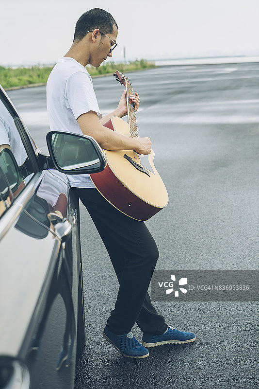 倚靠在汽车上的年轻男子弹吉他图片素材