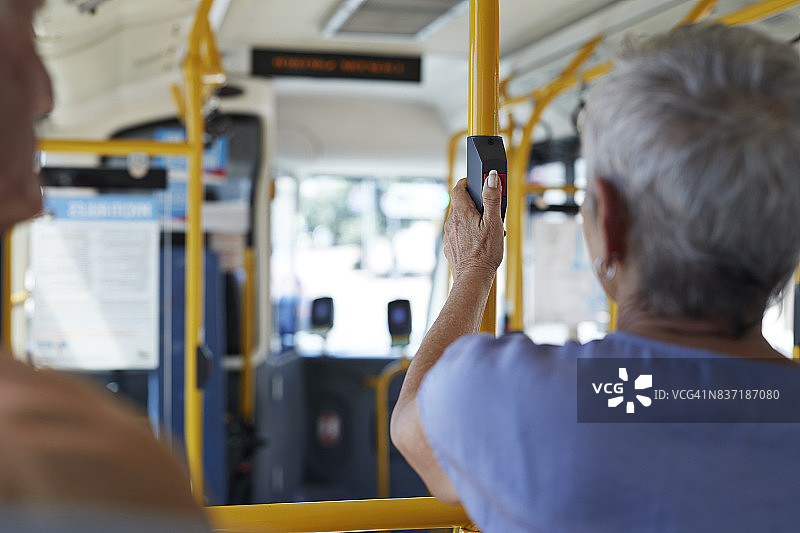 年长的男人在公共汽车内按下“停止”按钮图片素材