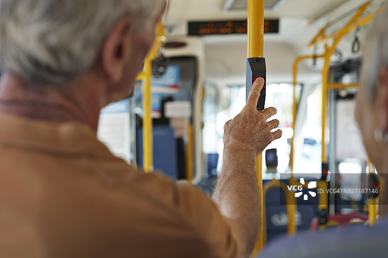 年长的男人在公共汽车内按下“停止”按钮图片素材