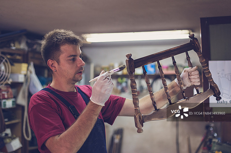 年轻木匠油漆婴儿床图片素材