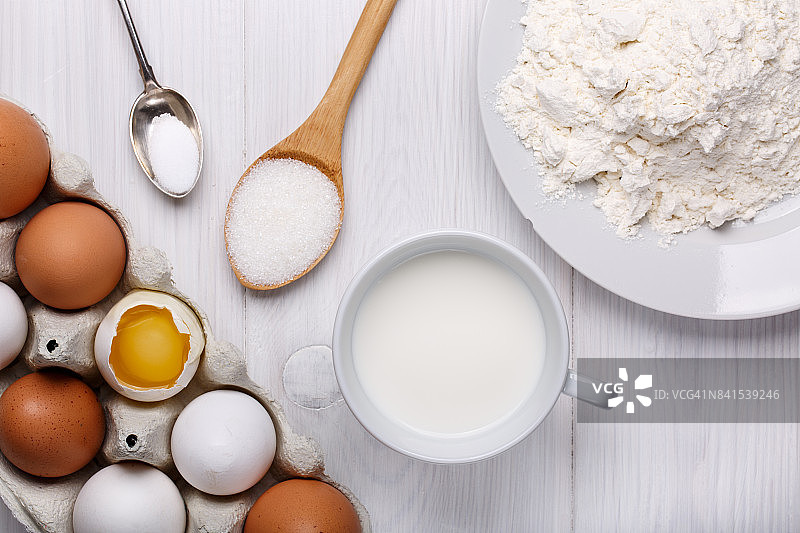 制作煎饼面团的食材：鸡蛋、面粉、牛奶、糖和盐（白色木桌，俯视）图片素材