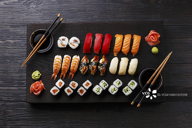 黑色木质背景上木制托盘中的寿司套餐：握寿司和寿司卷图片素材