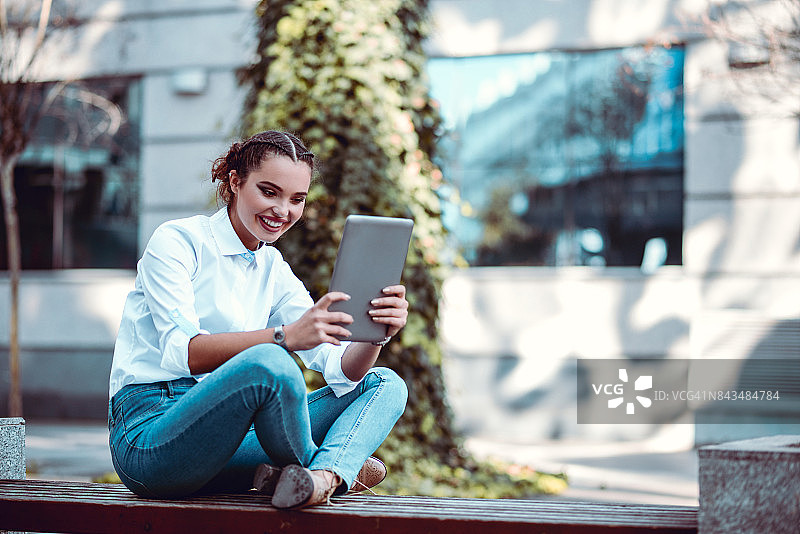 在城市长椅上使用平板电脑的微笑女性图片素材