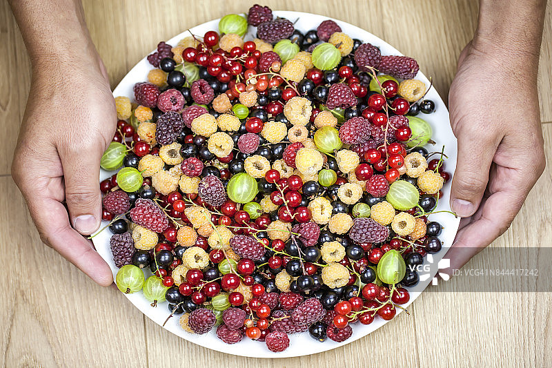 男人手持什锦健康食品盘，白色盘子上放着夏季浆果水果图片素材