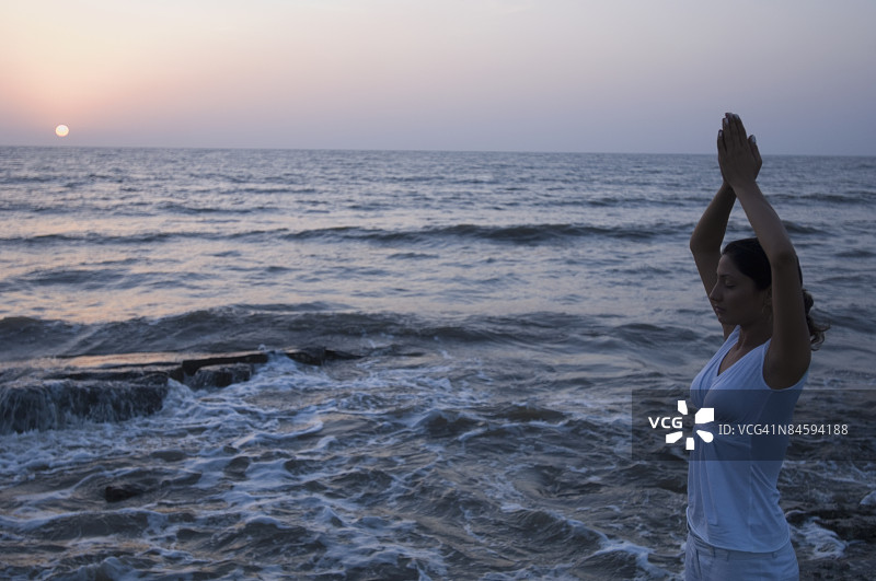 年轻女人在印度马哈拉施特拉邦孟买的穆德岛海滩上冥想的侧面照图片素材