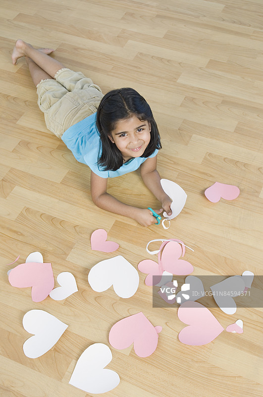 一个女孩在剪心形纸张，面带微笑的肖像图片素材