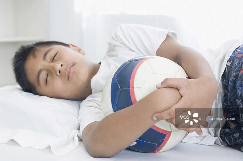 男孩在床上睡觉，手里抱着一个足球图片素材