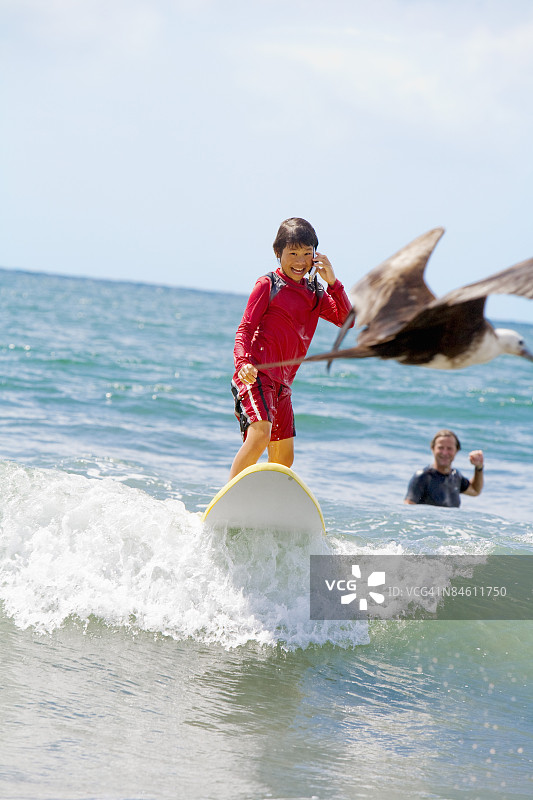 女孩在海中冲浪并用手机通话图片素材