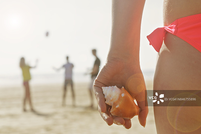 女人拿着贝壳，朋友们在海滩上玩耍图片素材