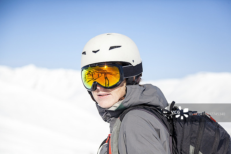 佩戴滑雪头盔、护目镜和背包的年轻女子，背景是蓝天和雪山图片素材