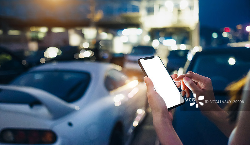 在户外停车场走向她的车时使用智能手机的女人图片素材