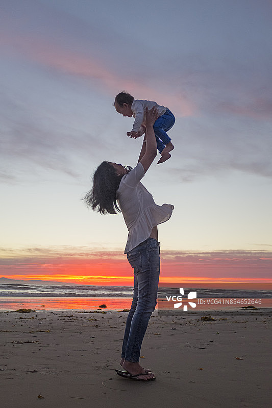 母亲在海滩上将她的女婴高高举起图片素材