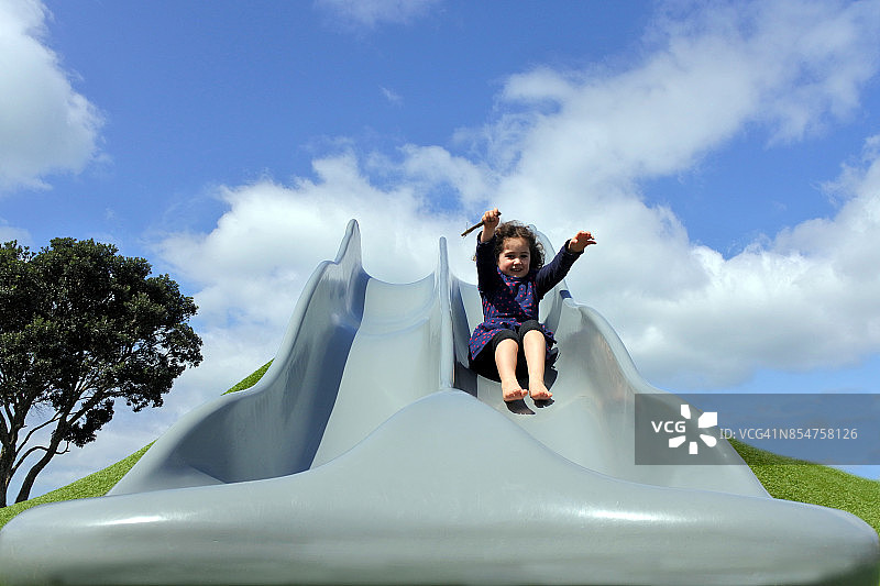 快乐的小女孩在操场上滑大滑梯图片素材