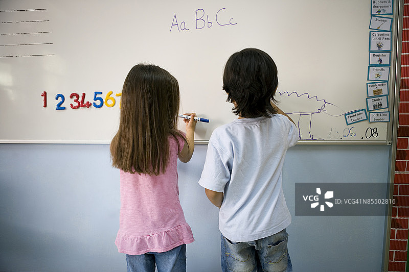 一位年轻女孩和男孩在教室的白板上写字图片素材