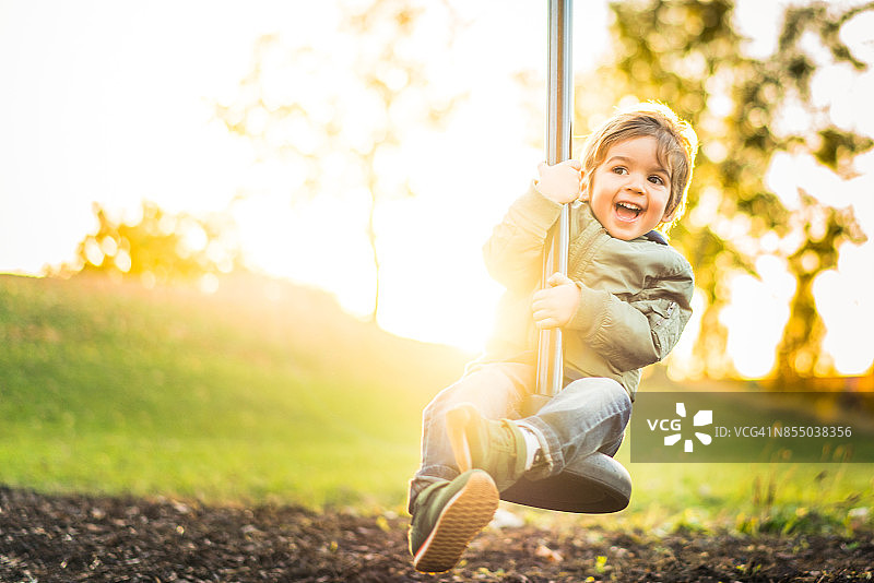 阳光明媚中，快乐的小男孩玩滑索图片素材