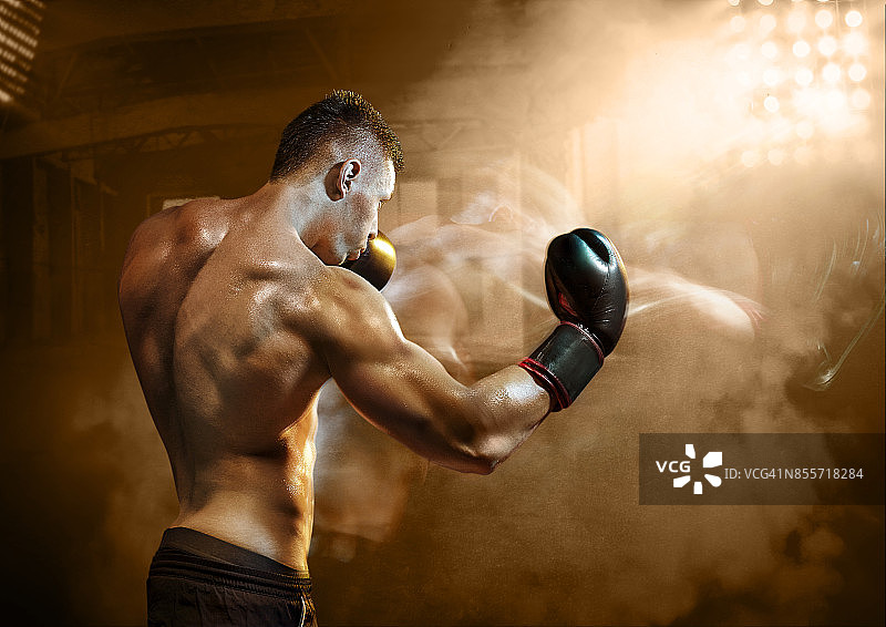 拳击手在光线充足的拳击馆里出拳，背景是昏暗的仓库图片素材