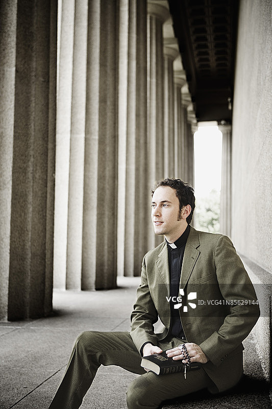 牧师坐在台阶上，手持圣经和念珠图片素材