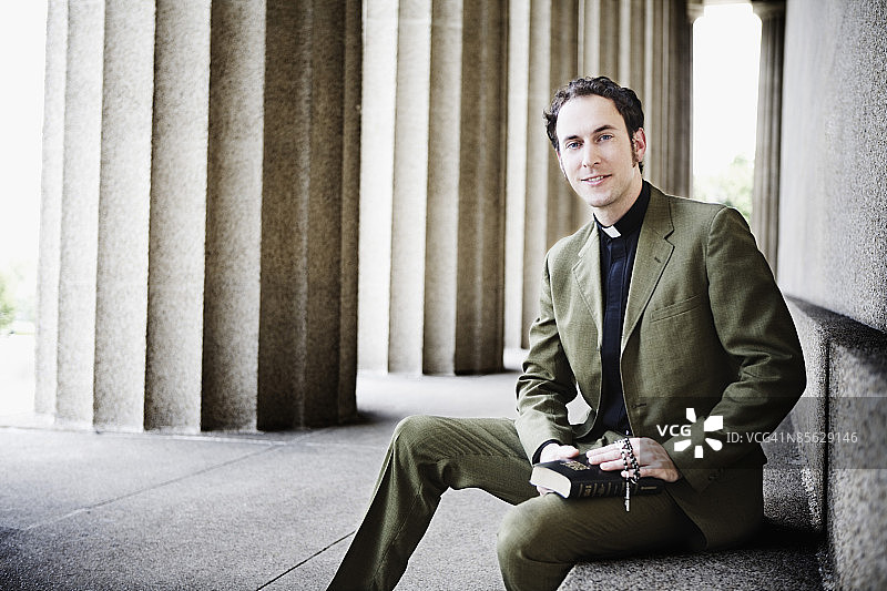 牧师坐在台阶上，手持圣经和念珠图片素材