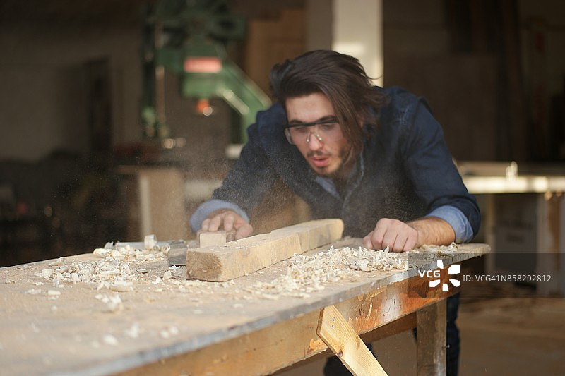 英俊的年轻木匠吹掉锯末图片素材