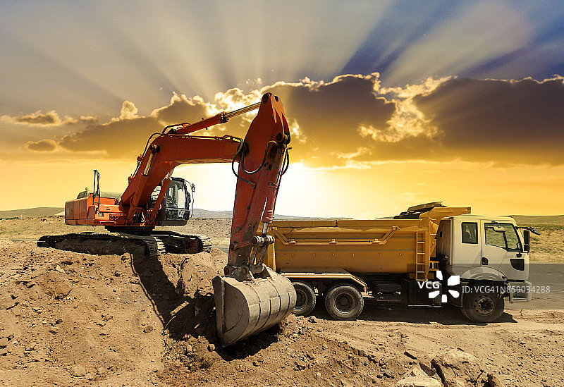 日落时分挖掘机装载自卸卡车图片素材