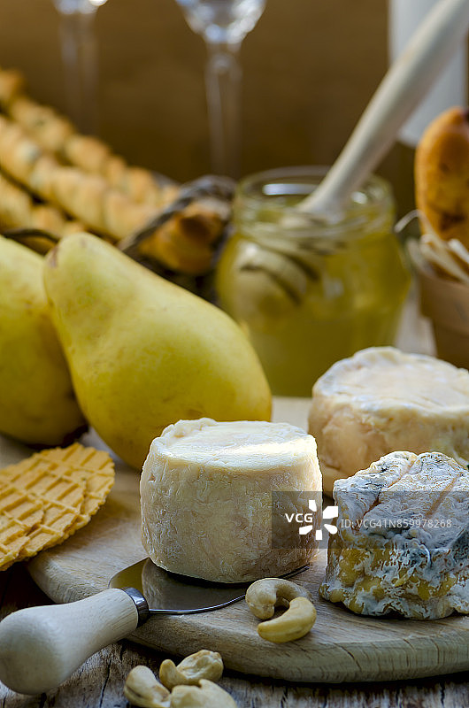 法国手工山羊奶酪配梨、面包棒、华夫饼、蜂蜜、白葡萄酒和腰果图片素材