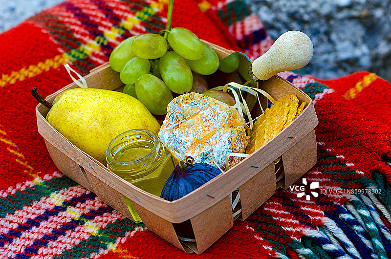 乌克兰制造的法国手工山羊奶酪Crottin de Chavignol配梨、无花果、蜂蜜、葡萄在篮子里放在石头上图片素材