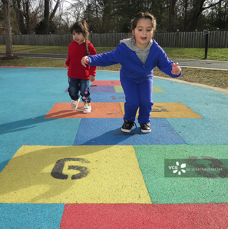 两姐妹在操场上玩跳房子游戏图片素材