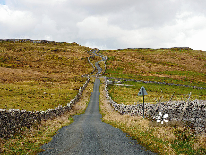 约克郡山谷中一条狭窄的蜿蜒道路，两旁是干燥的石墙图片素材