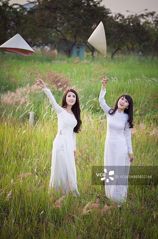 身穿奥黛的年轻漂亮女孩在芦苇草地背景下抛掷斗笠图片素材