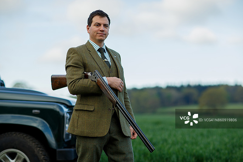 一个男人在飞碟射击场手持步枪，站在路虎车前图片素材