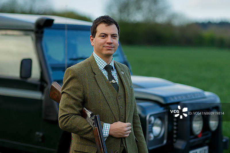 一个男人在飞碟射击场手持步枪，站在路虎车前图片素材