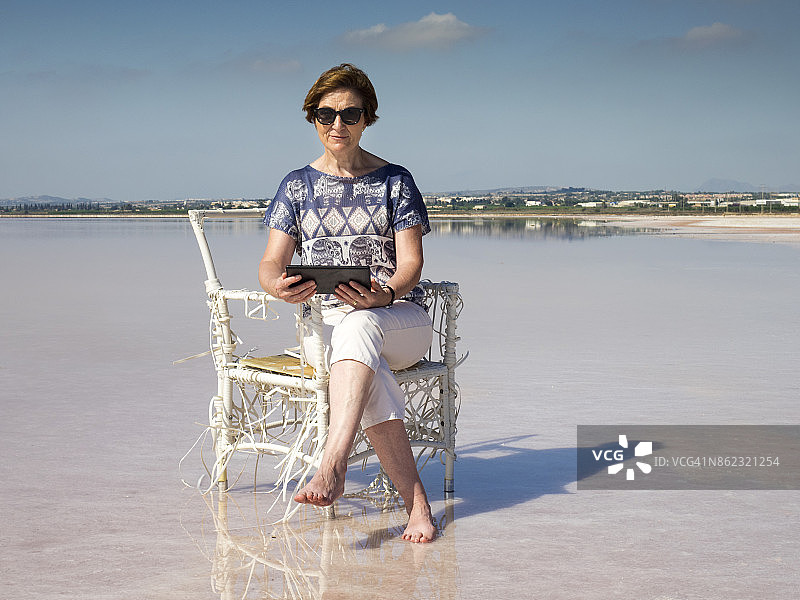 阳光下女人在湖边藤椅上阅读图片素材