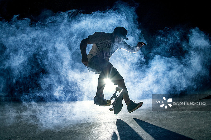 滑板少年在夜晚的烟雾和灯光中玩技巧图片素材
