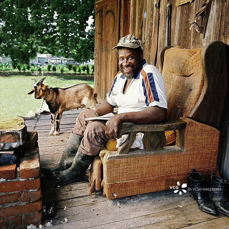 坐在门廊上，背景是他的宠物山羊的男人图片素材