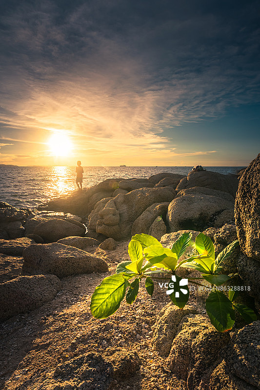 日落时分站在海滩上的男孩图片素材