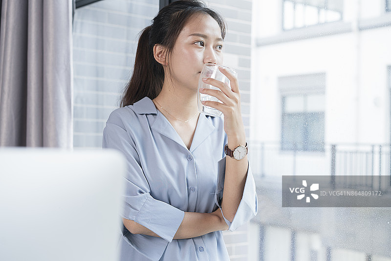 年轻女子倚靠在窗台上喝水图片素材