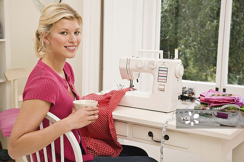 在缝纫机旁拿着咖啡杯摆姿势的女人图片素材