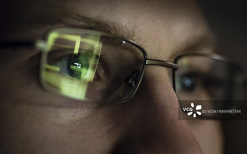 年轻黑客肖像，电脑屏幕在眼镜中反射图片素材