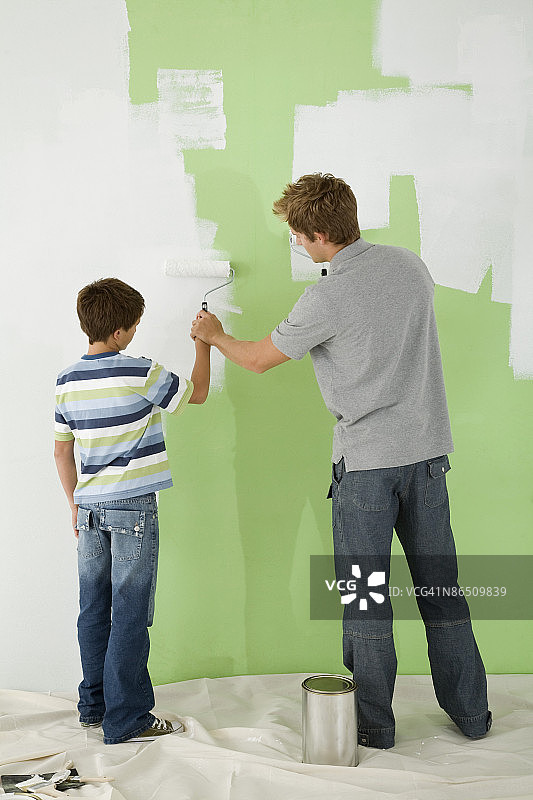 父亲帮助儿子粉刷墙壁图片素材