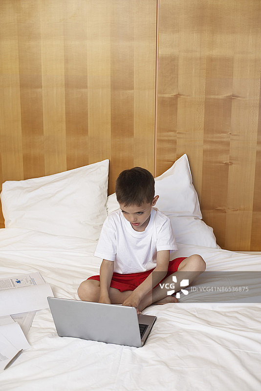 男孩在床上使用笔记本电脑图片素材