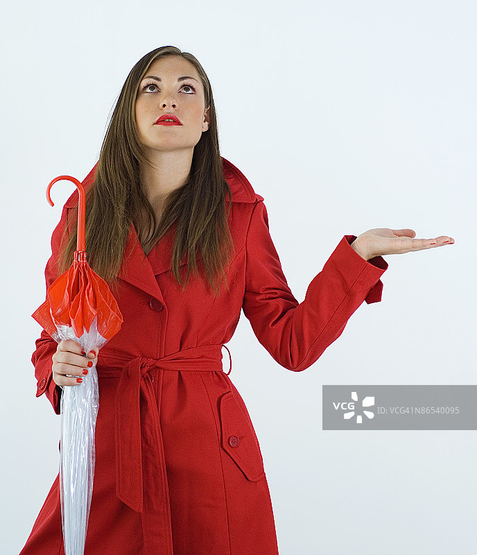 穿红色风衣，拿着雨伞，期盼下雨的女人图片素材