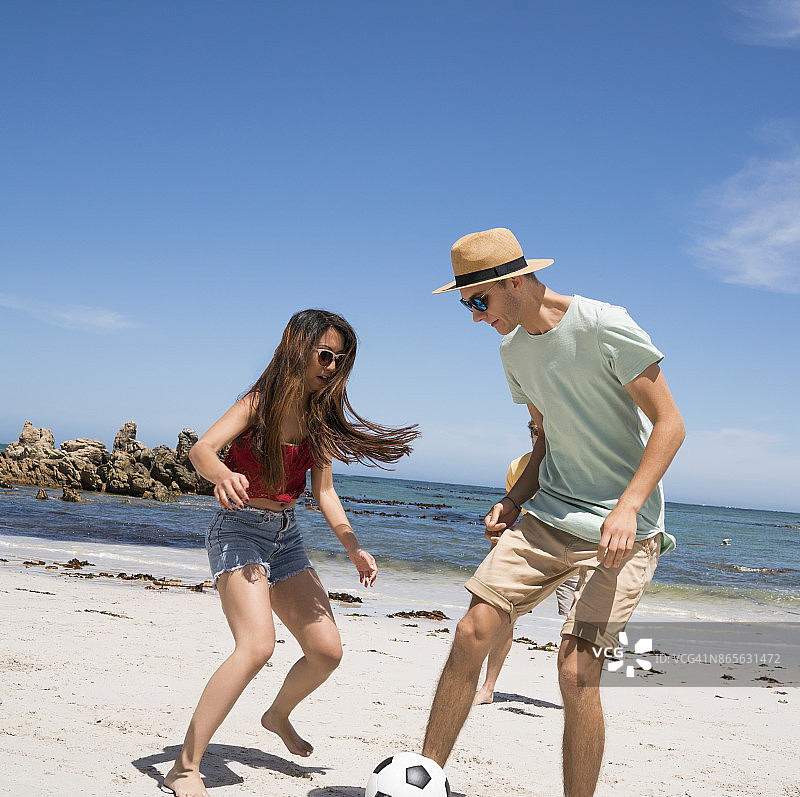 在海滩上踢足球的年轻男人和女人图片素材