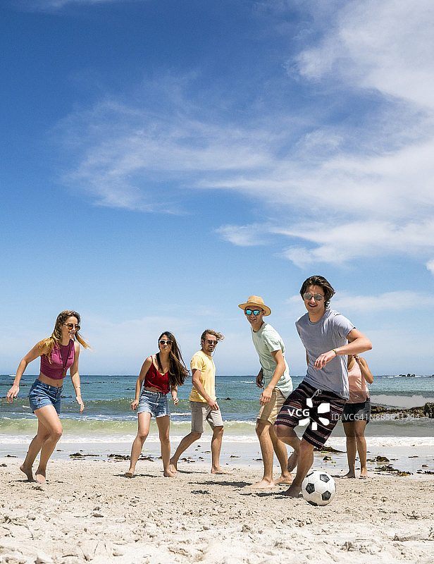 在海滩上和朋友踢足球的年轻男人图片素材