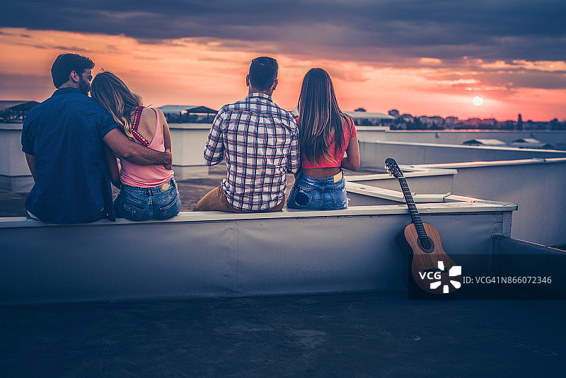日落时分坐在屋顶上的两对情侣的背影图片素材